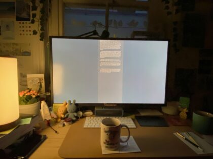 Desk with big monitor, lit from the left. A mug sits in front of the keyboard.