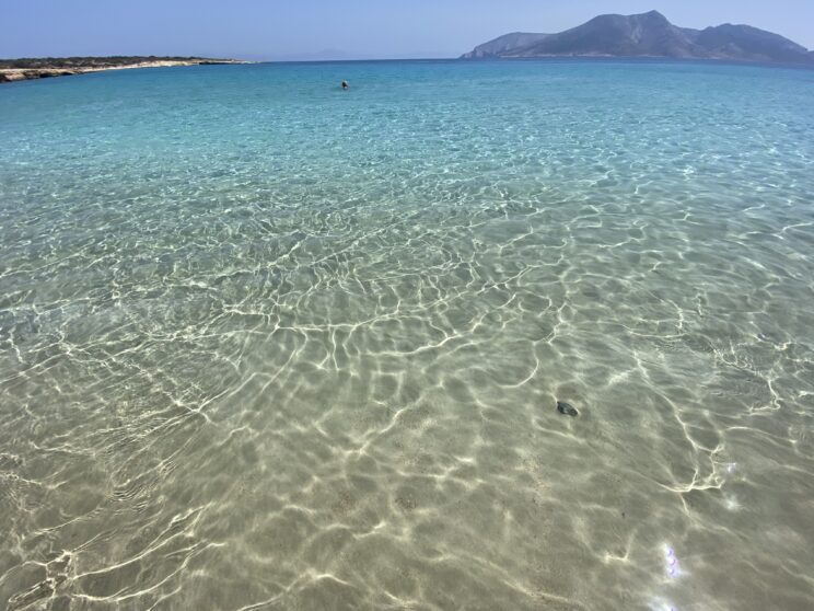 Photo of the sea, water coloured from sandy to turquoise and an island in the distance